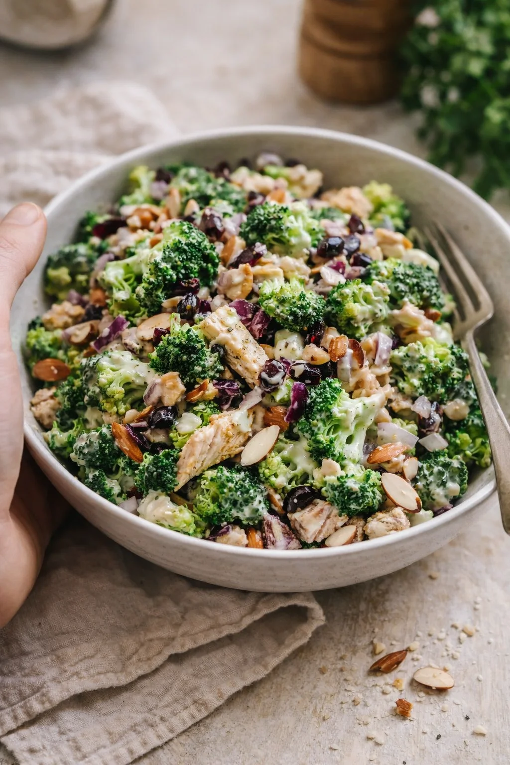 Broccoli florets, diced chicken, almonds, and red onions in a creamy dressing in a gray bowl.