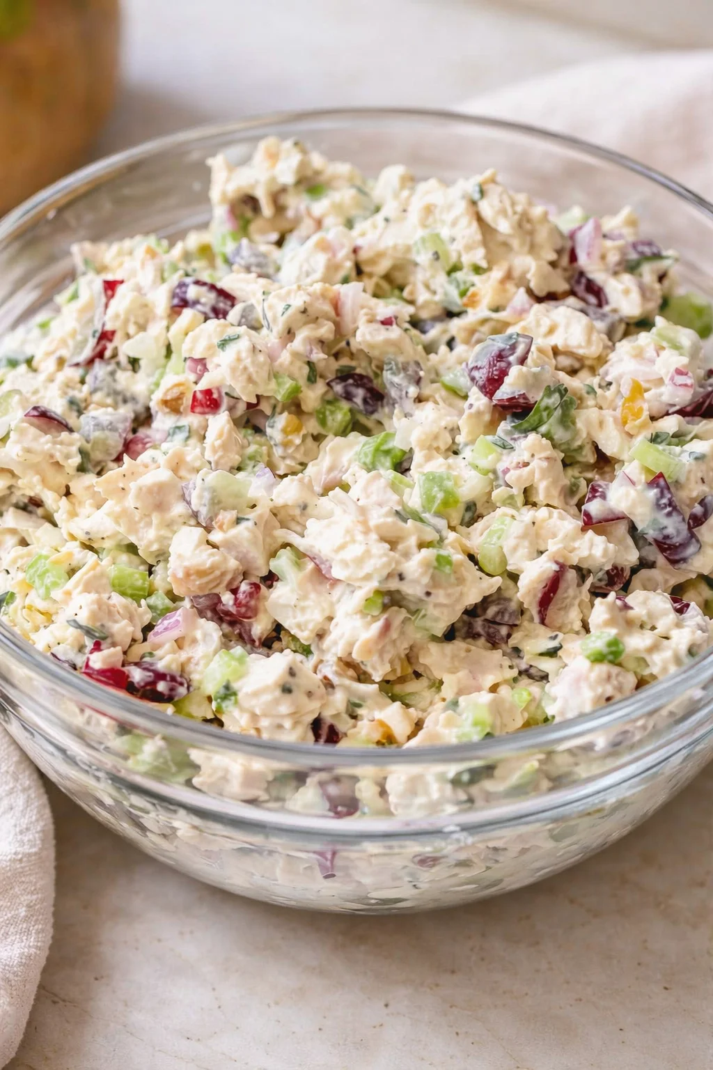 glass bowl of creamy chicken salad with celery, red grapes, and herbs