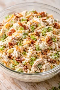 Creamy chicken salad with peas, bacon, and carrot in a clear glass bowl