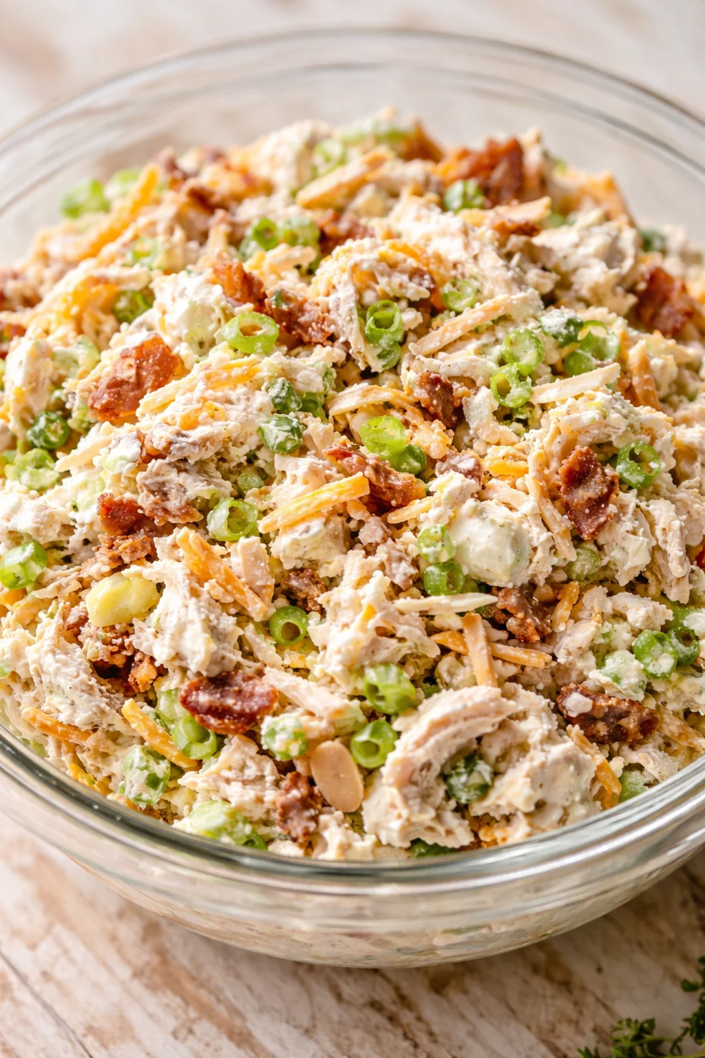 Creamy chicken salad with peas, bacon, and carrot in a clear glass bowl