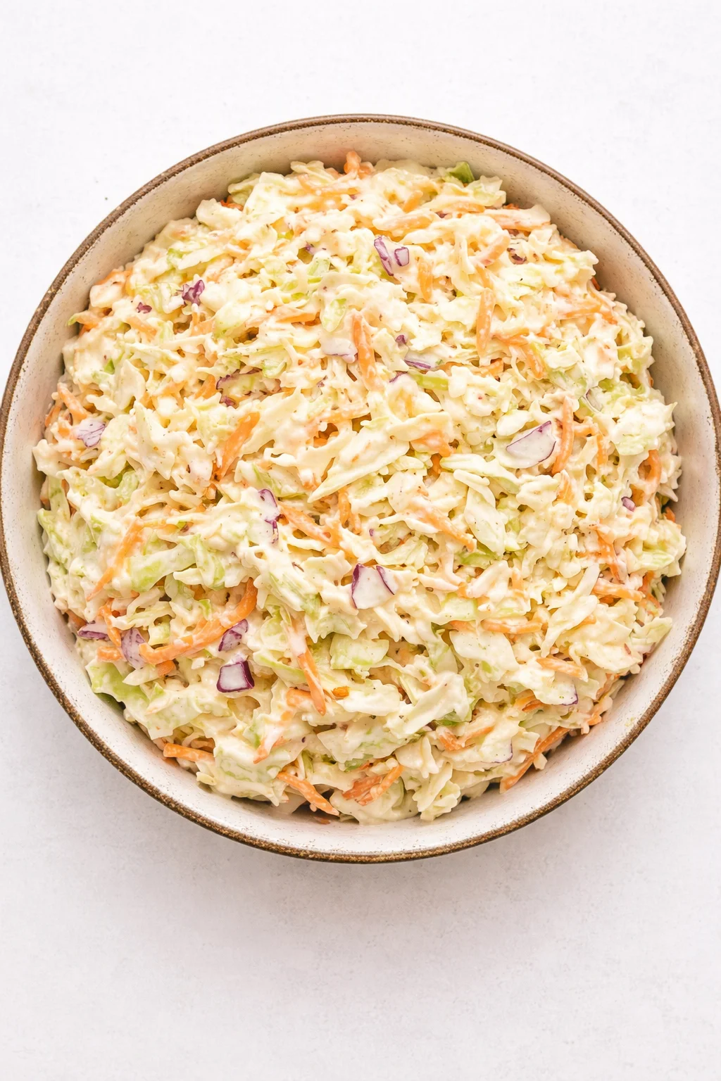 Top-down view of a bowl of creamy coleslaw with shredded cabbage, carrots, and red onion.