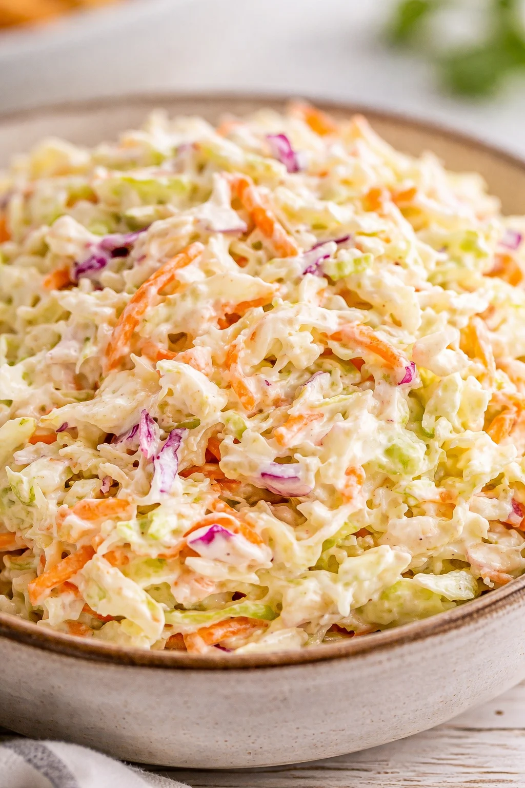 Creamy coleslaw with shredded cabbage, carrots, and red onion in a rustic ceramic bowl