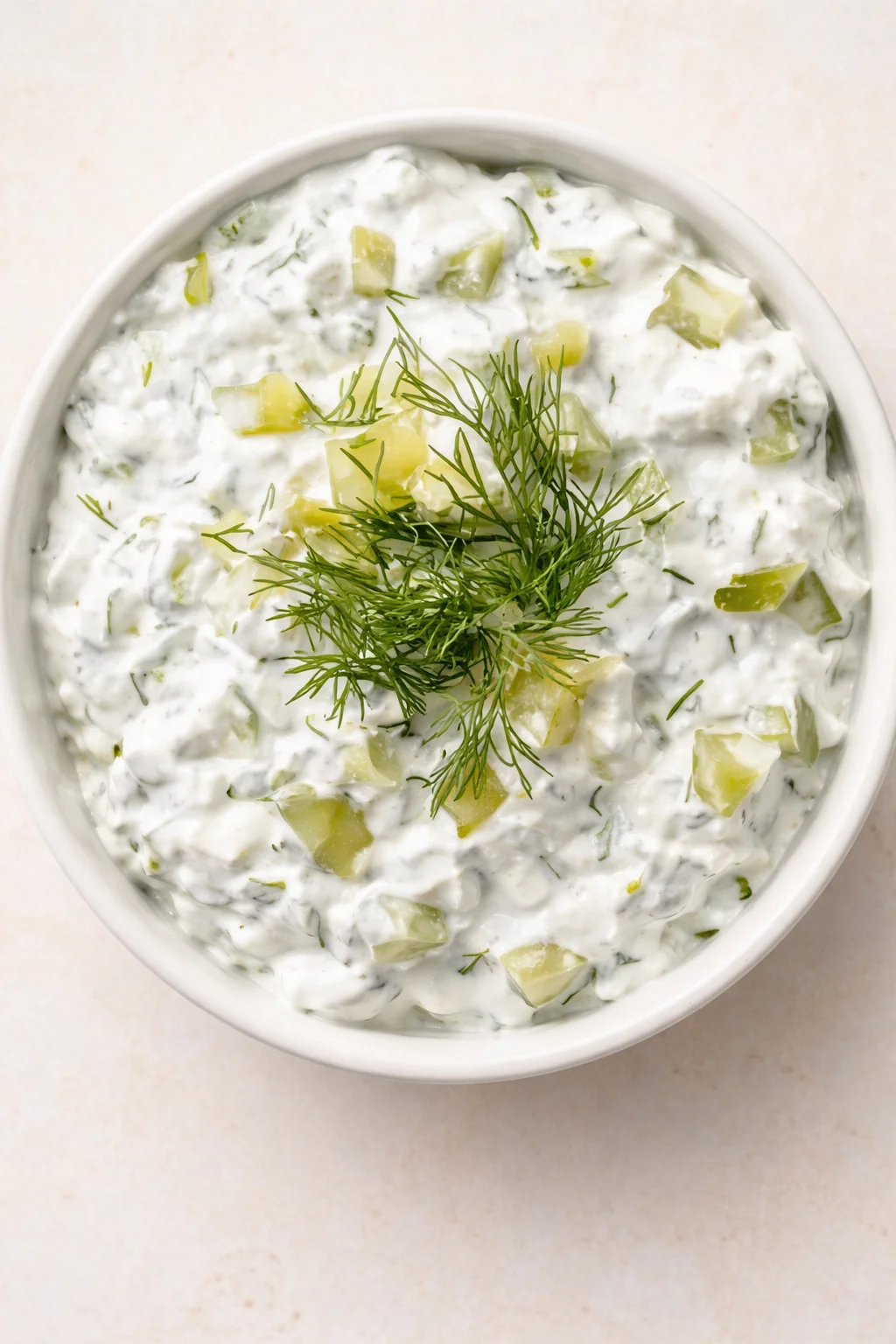 top-down view of a creamy cucumber-dill dip in a white bowl, garnished with dill