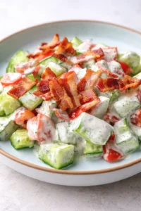 creamy cucumber tomato salad with crispy bacon on a pale blue plate