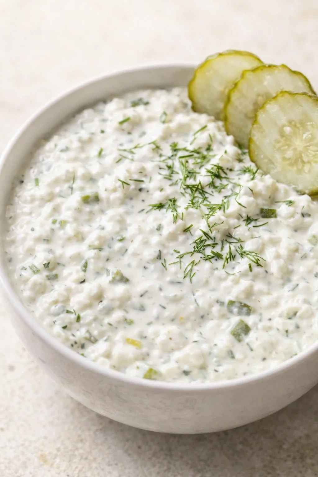 Creamy yogurt-dill dip with cucumber pieces in a white bowl, garnished with dill and cucumber rounds.