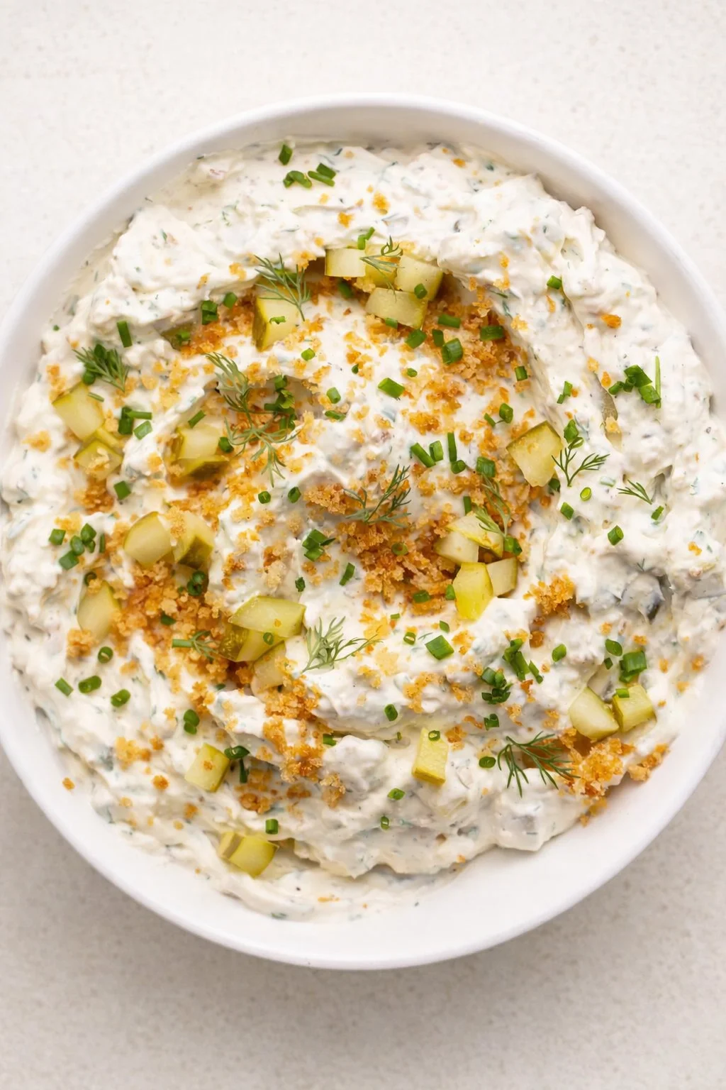 Creamy white herbed dip in a bowl, garnished with dill, chives, cucumber cubes, and crunchy crumbs.