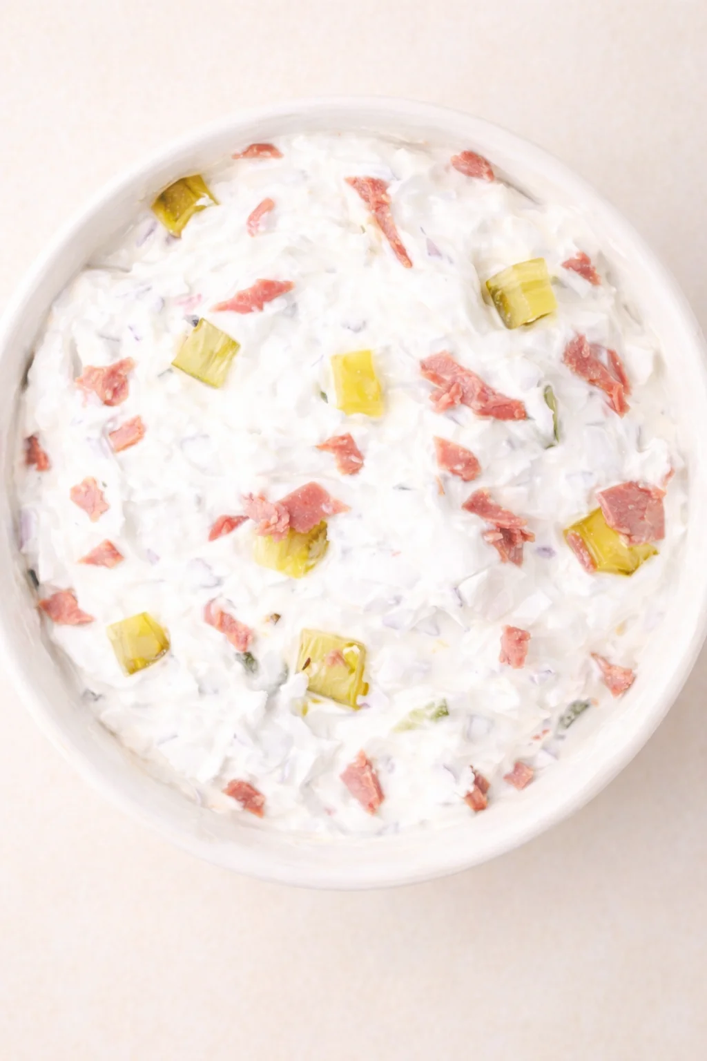 top-down view of a white bowl filled with creamy ham and pickle salad with onion bits.