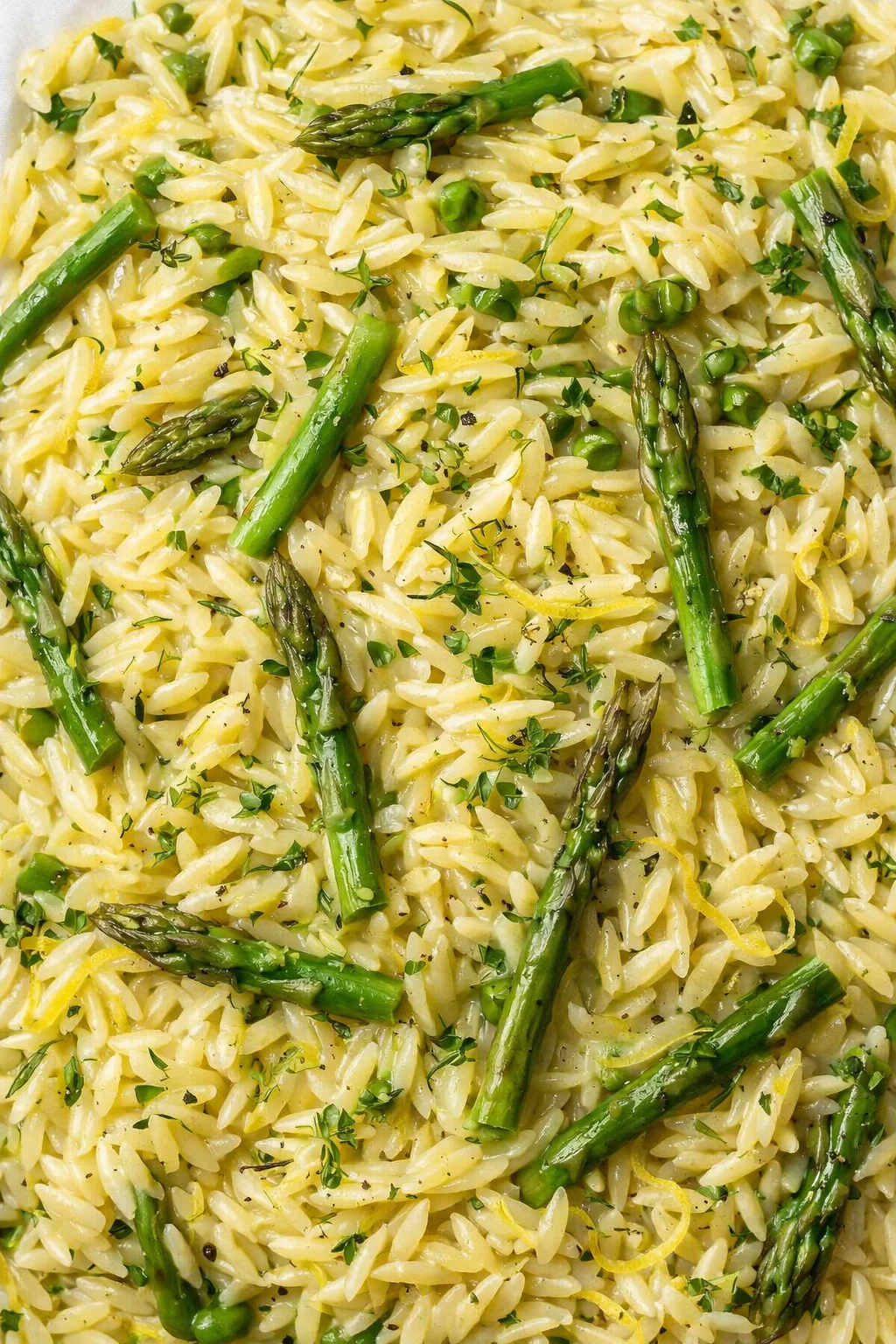 Close-up of creamy lemon-parmesan orzo with asparagus spears, peas, and chopped herbs.