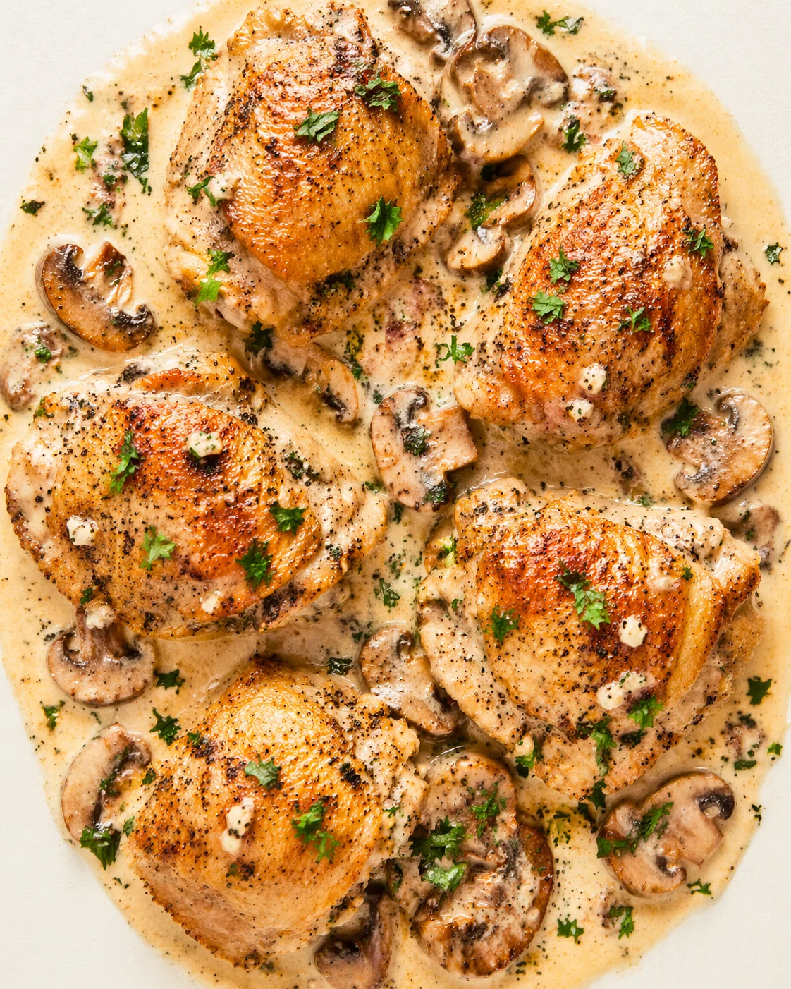 several golden-brown chicken pieces in creamy mushroom sauce, garnished with parsley