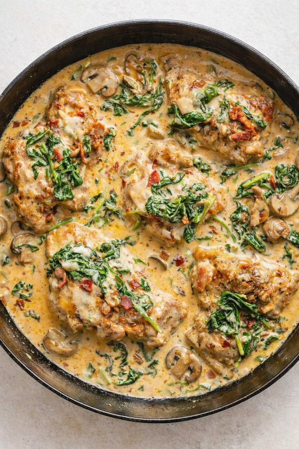 Cast-iron skillet filled with creamy chicken, mushrooms, bacon, and wilted spinach.
