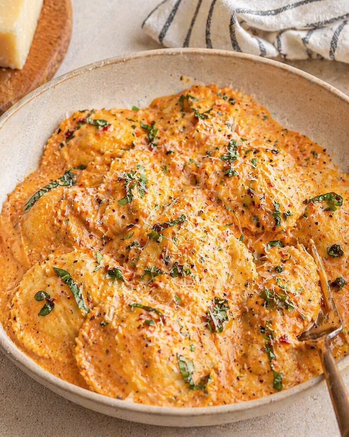Creamy parmesan ravioli in a beige bowl, topped with herbs and grated cheese.