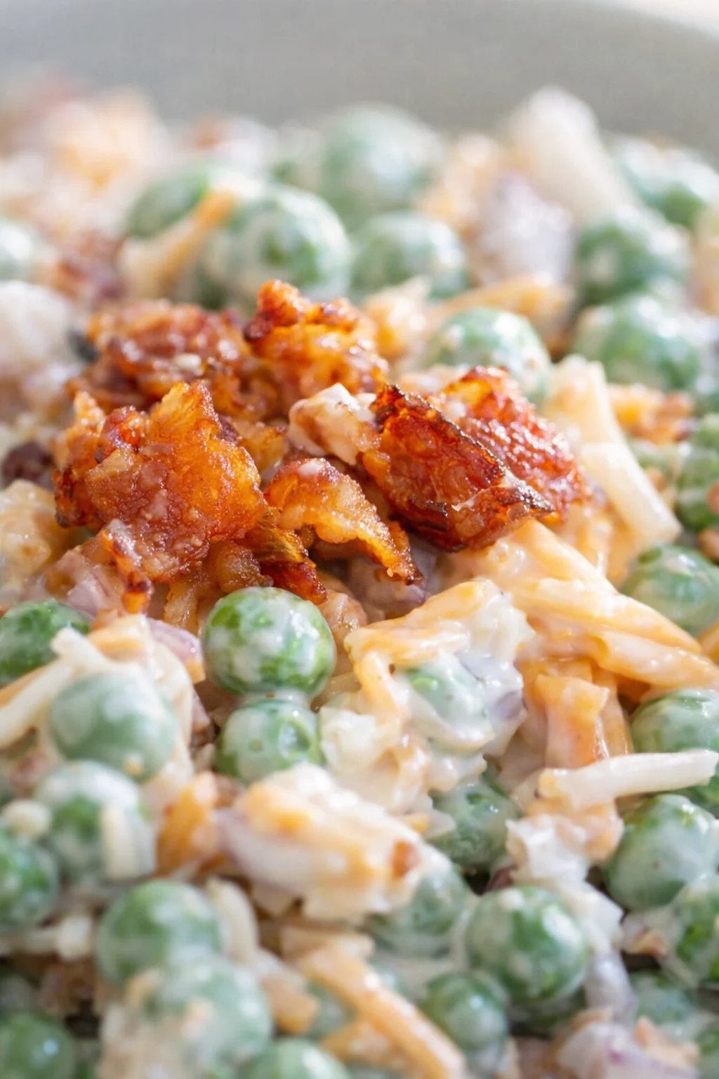 Close-up of creamy pea-bacon dish with melted cheese and crispy bacon on top.