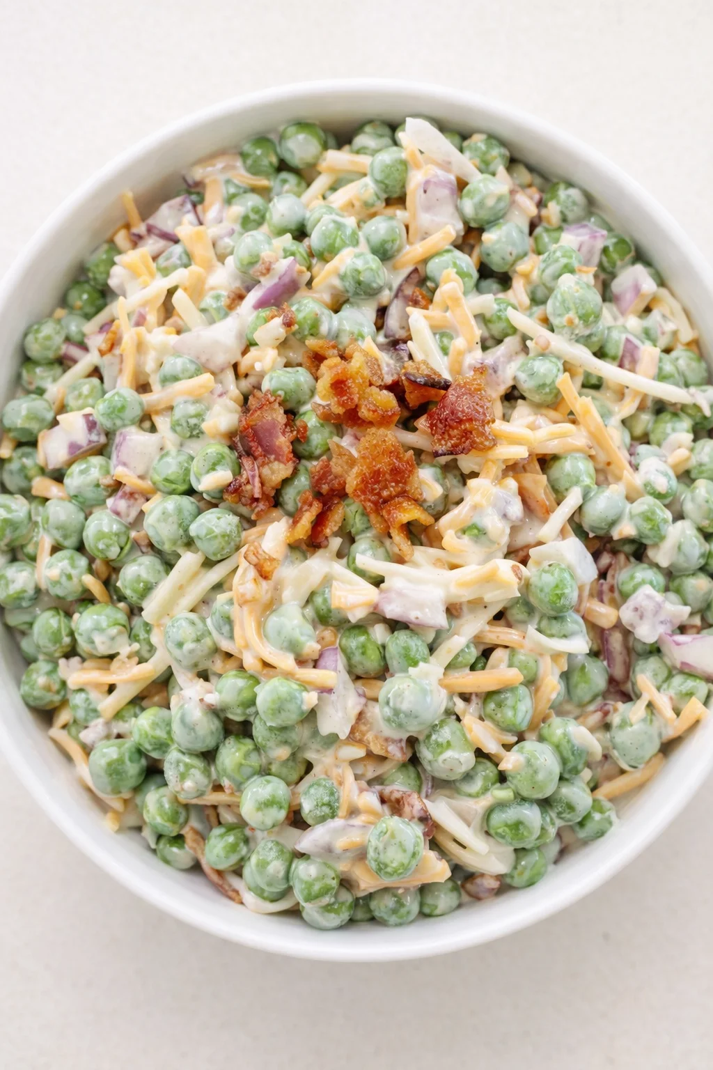 bowl of creamy pea salad with bacon, onions, and shredded cheddar