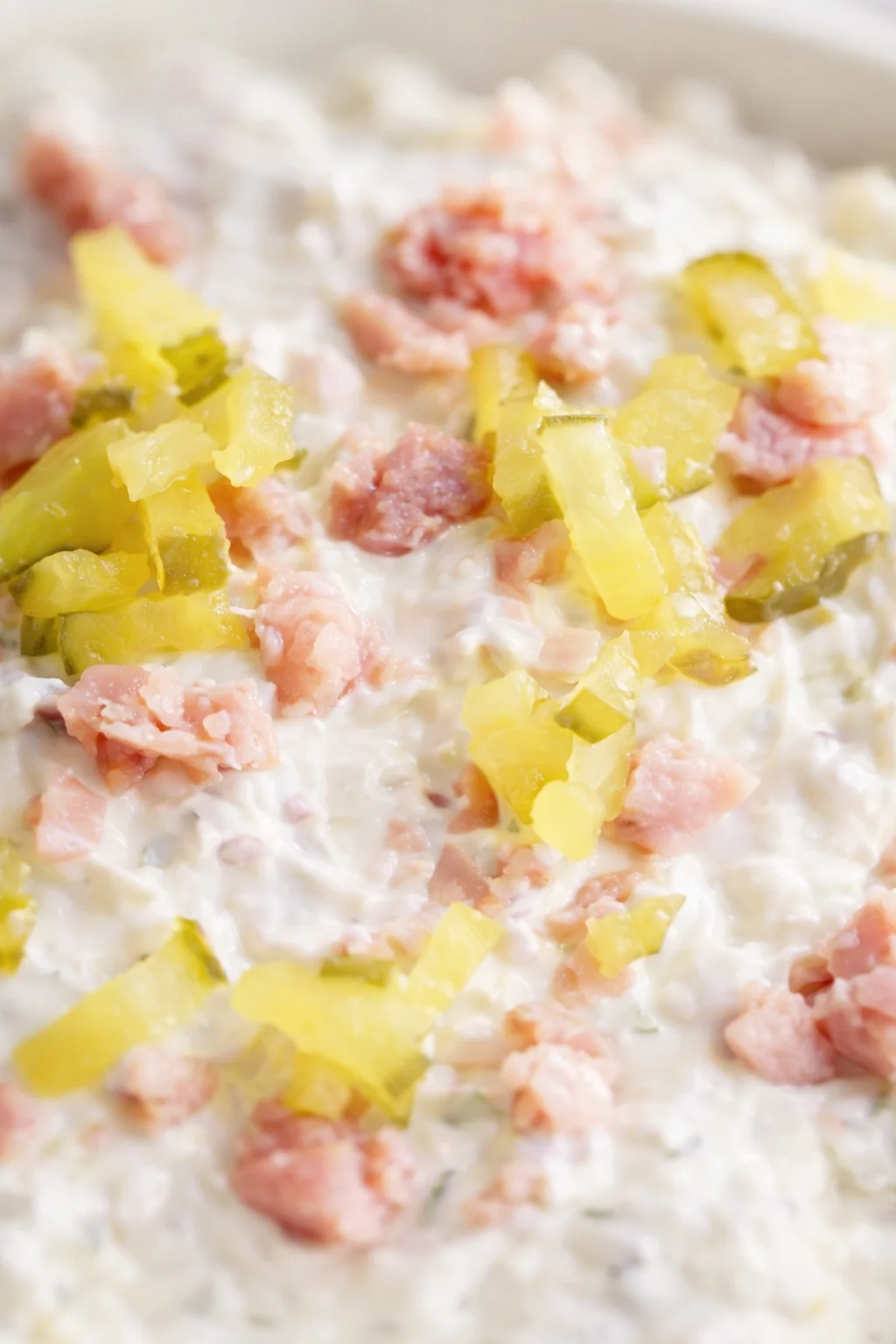 Close-up of a creamy white dressing with pink ham chunks and yellow pineapple pieces.