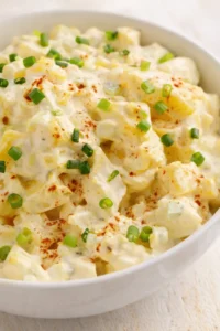Close-up of creamy potato salad with potato cubes, mayo dressing, and chopped green onions in a white bowl.