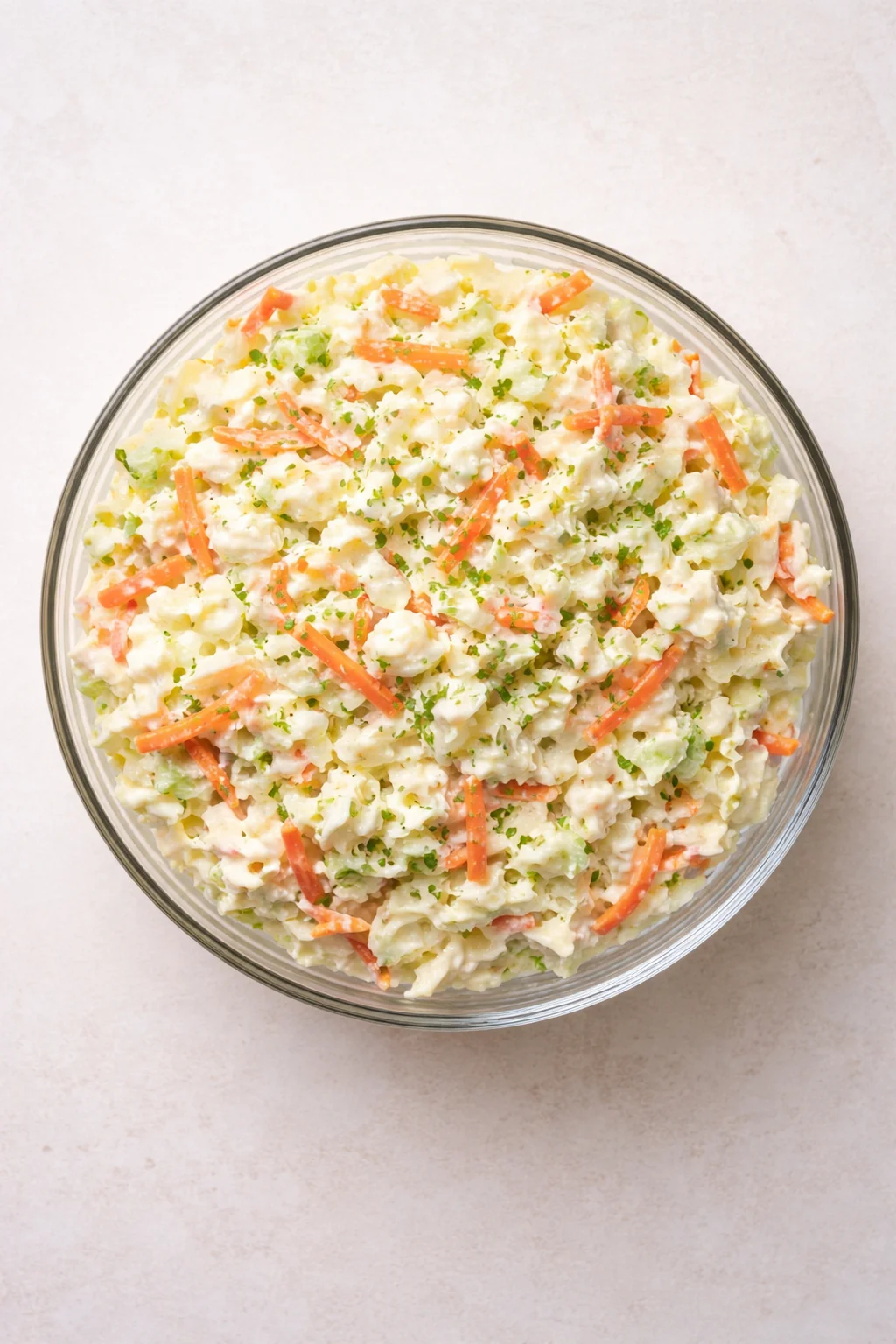 top-down view of creamy potato salad in a glass bowl with carrot sticks and herbs