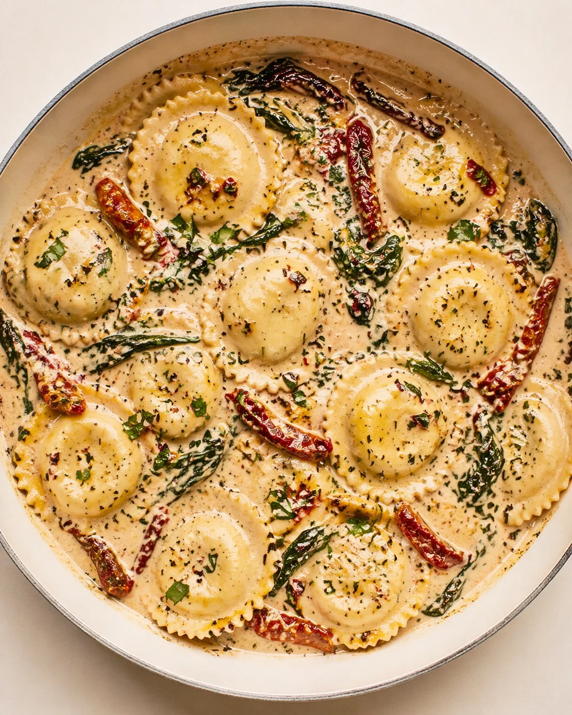 Creamy ravioli in a skillet, topped with herbs and red chili strips