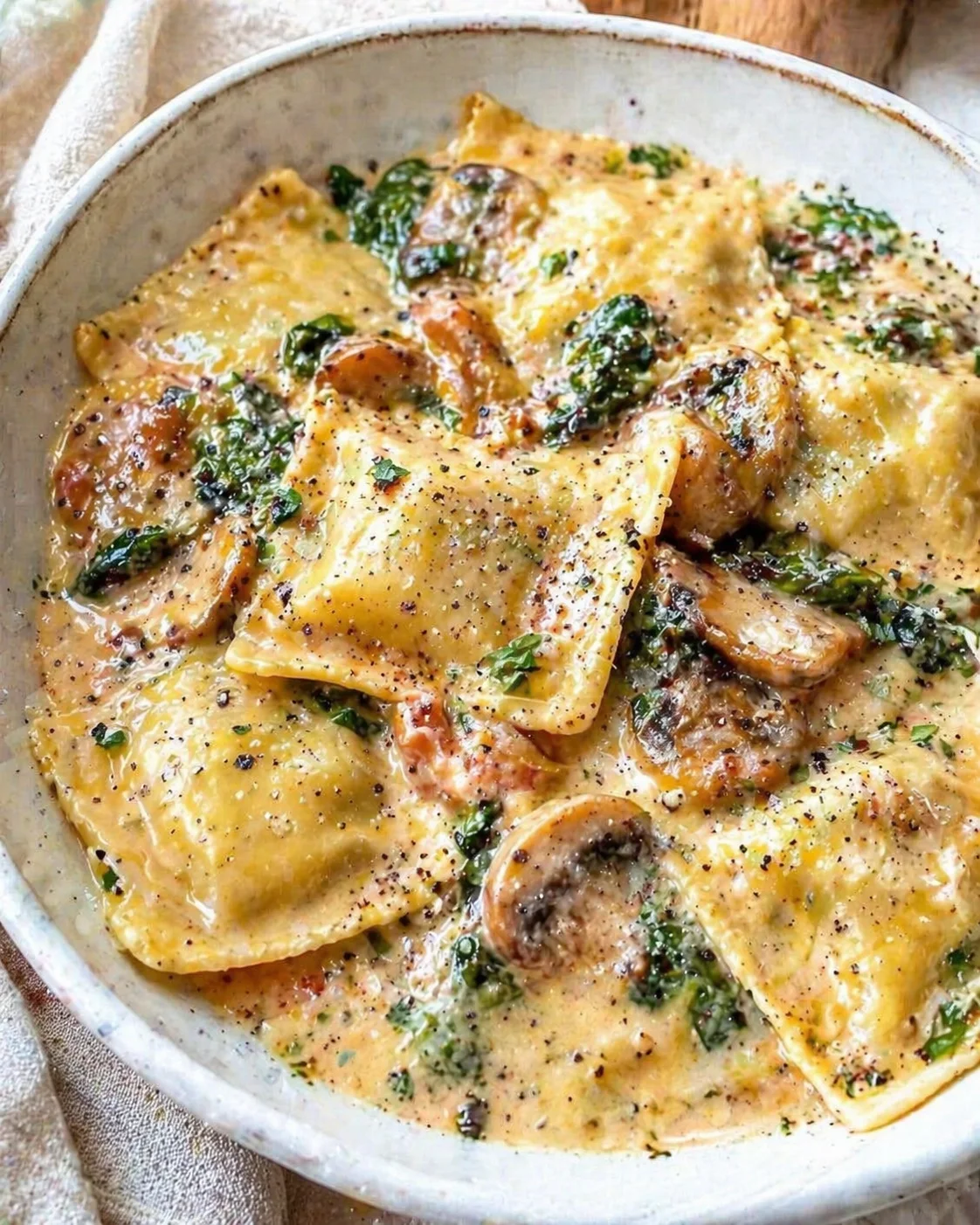 Creamy ravioli with mushrooms and herbs in a shallow ceramic dish.