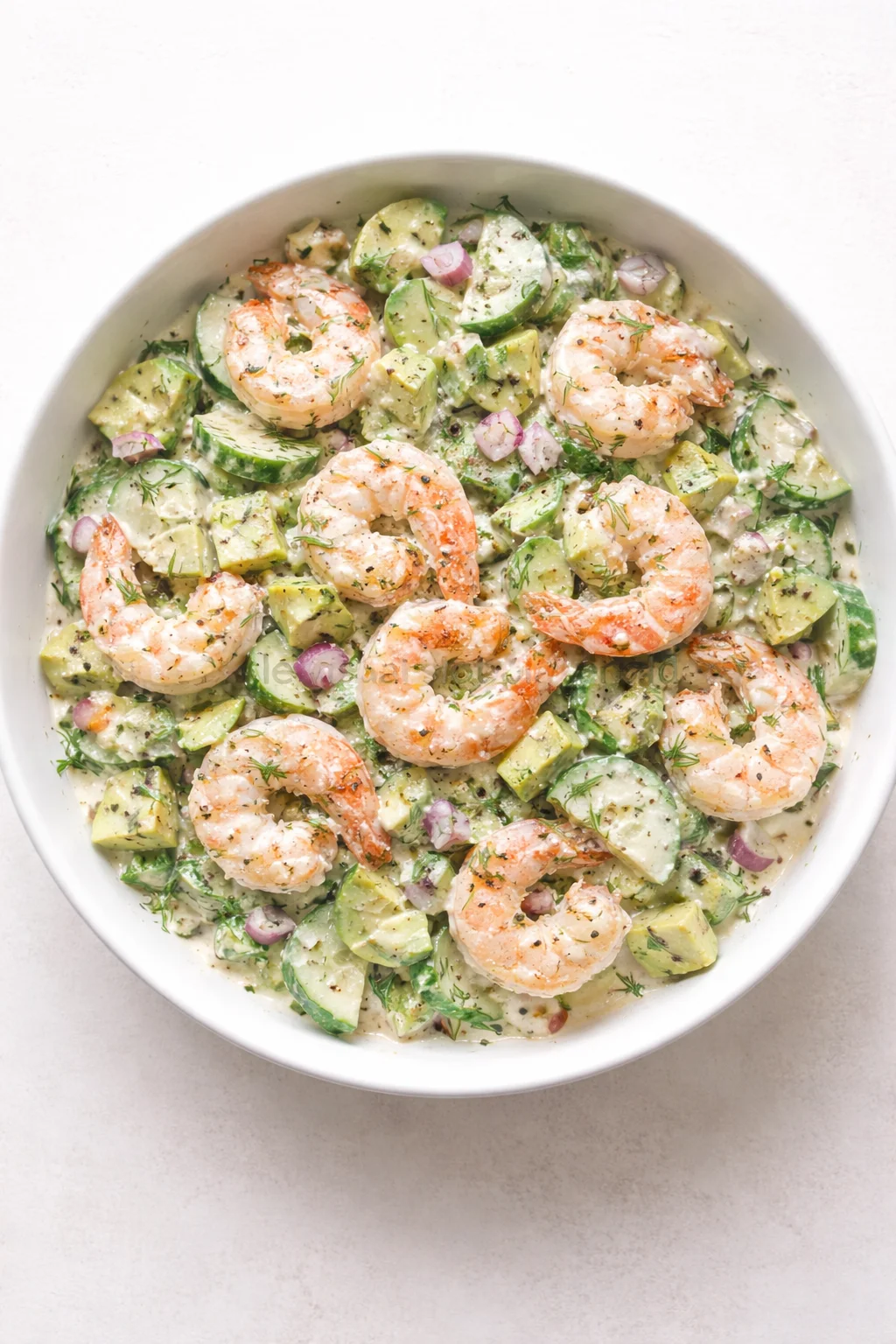 bowl of creamy shrimp salad with avocado, cucumber, and dill