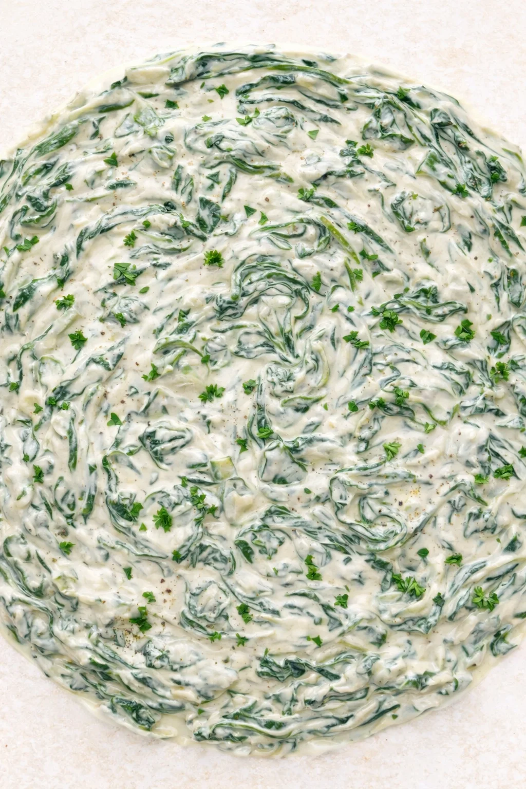 Creamy spinach-artichoke dip swirled with greens, garnished with parsley on a light background