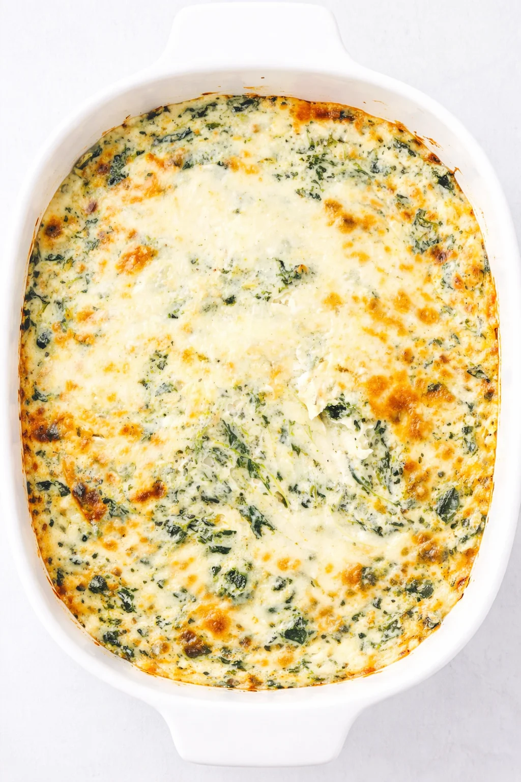 Creamy spinach and cheese bake with browned top in a white oval dish.