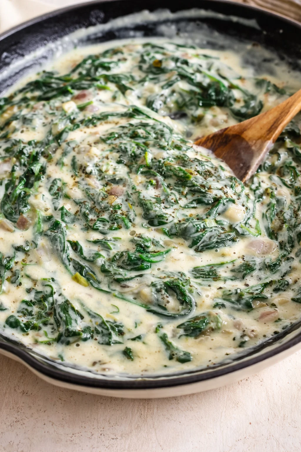 creamy spinach-sauce with wilted greens in a dark skillet and a wooden spoon