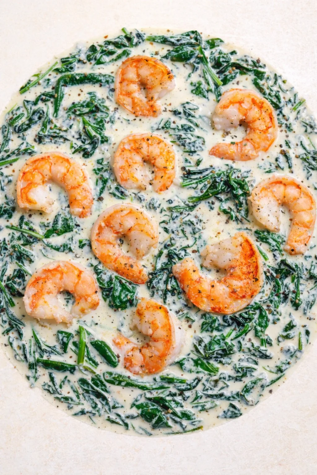 orange-pink shrimp arranged in a circle atop a white creamy spinach sauce with pepper specks.