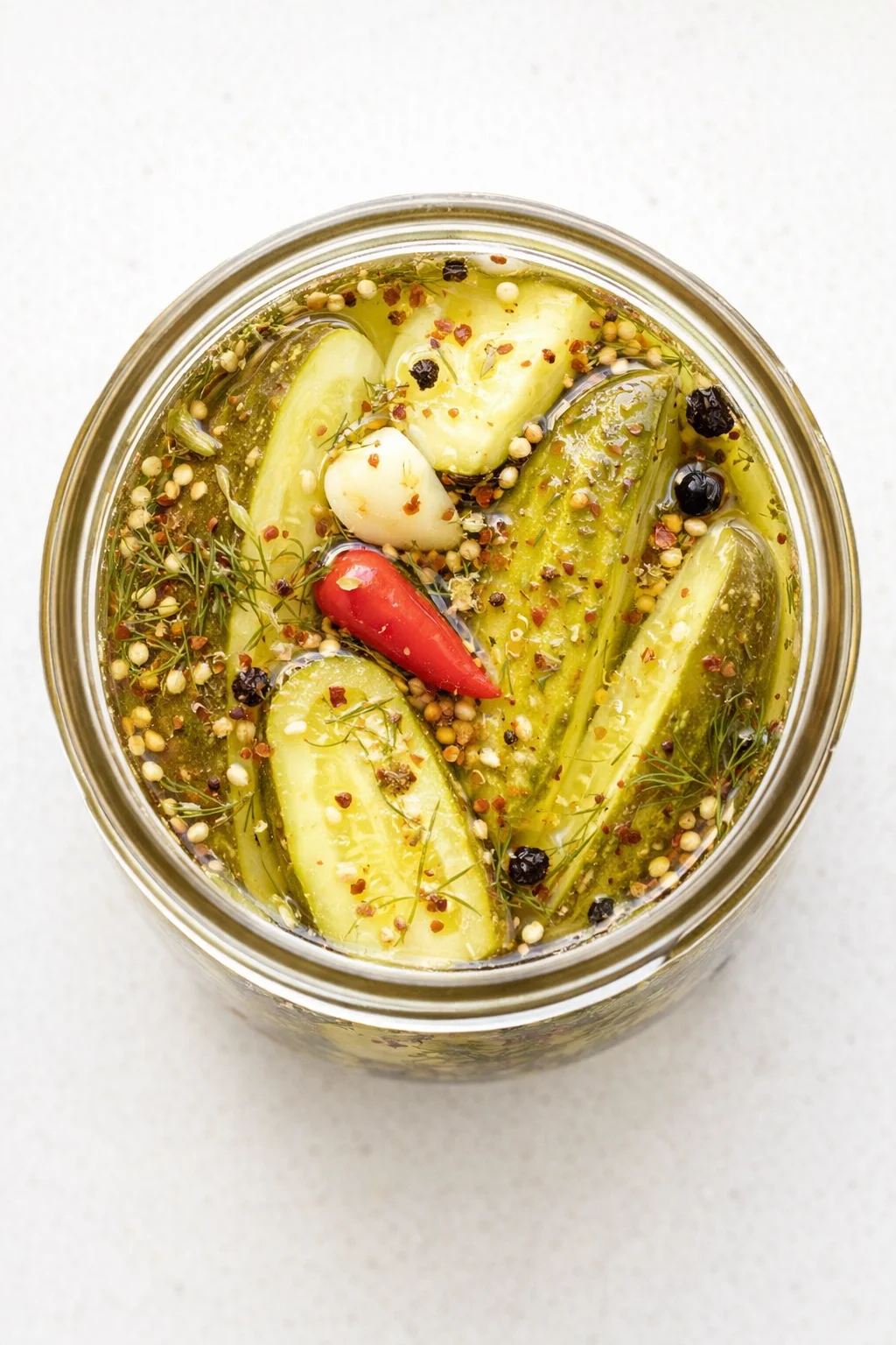 Top-down view of cucumber pickles in a glass jar with dill, garlic, and red chili in brine.
