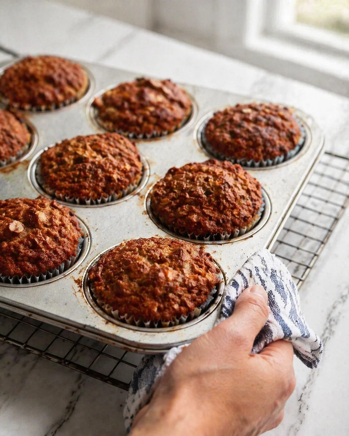 Tray of crumb-topped muffins cooling on a rack by a sunlit marble counter.