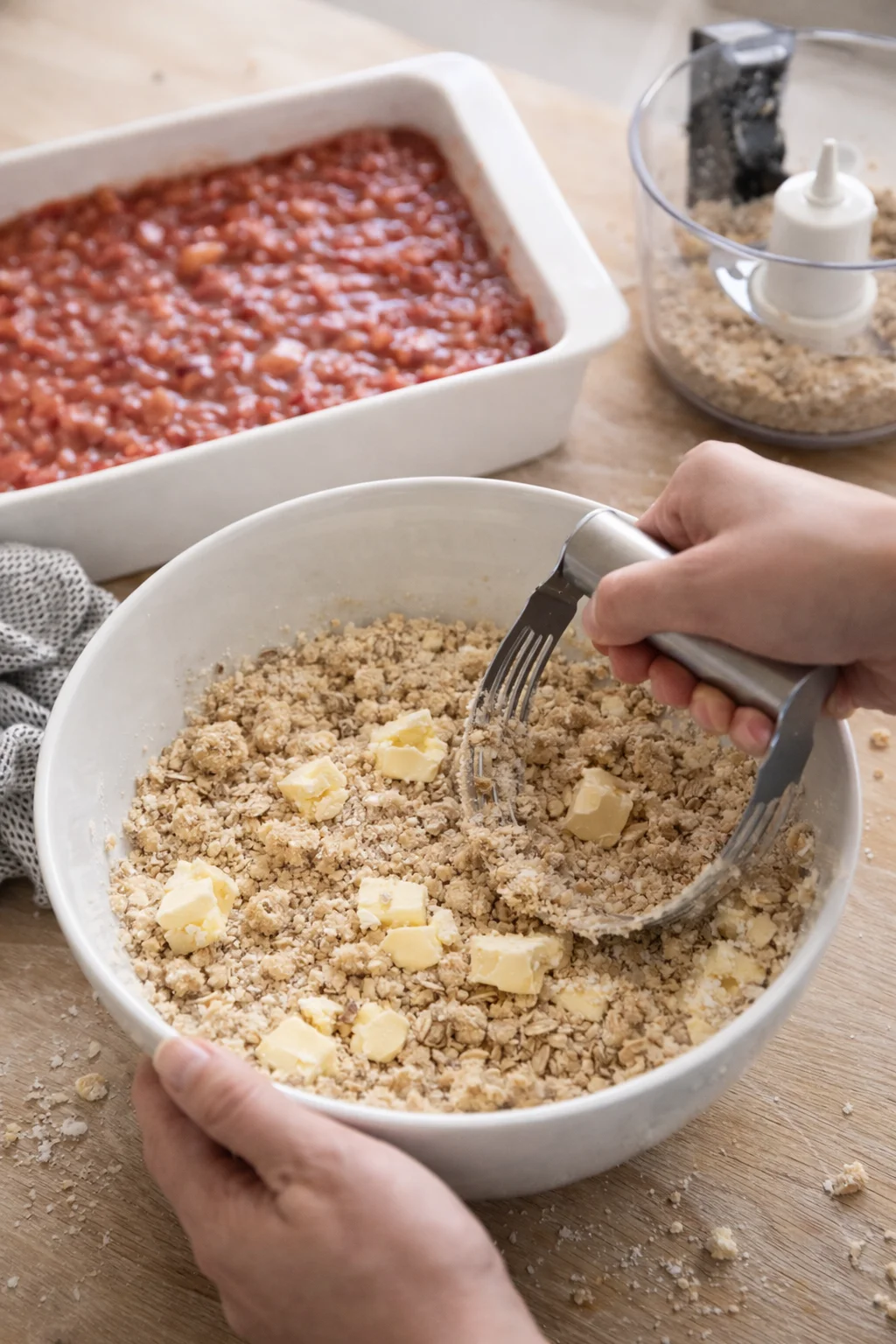 Hands cutting cold butter into oat-flour-sugar mixture until coarse crumbs form.