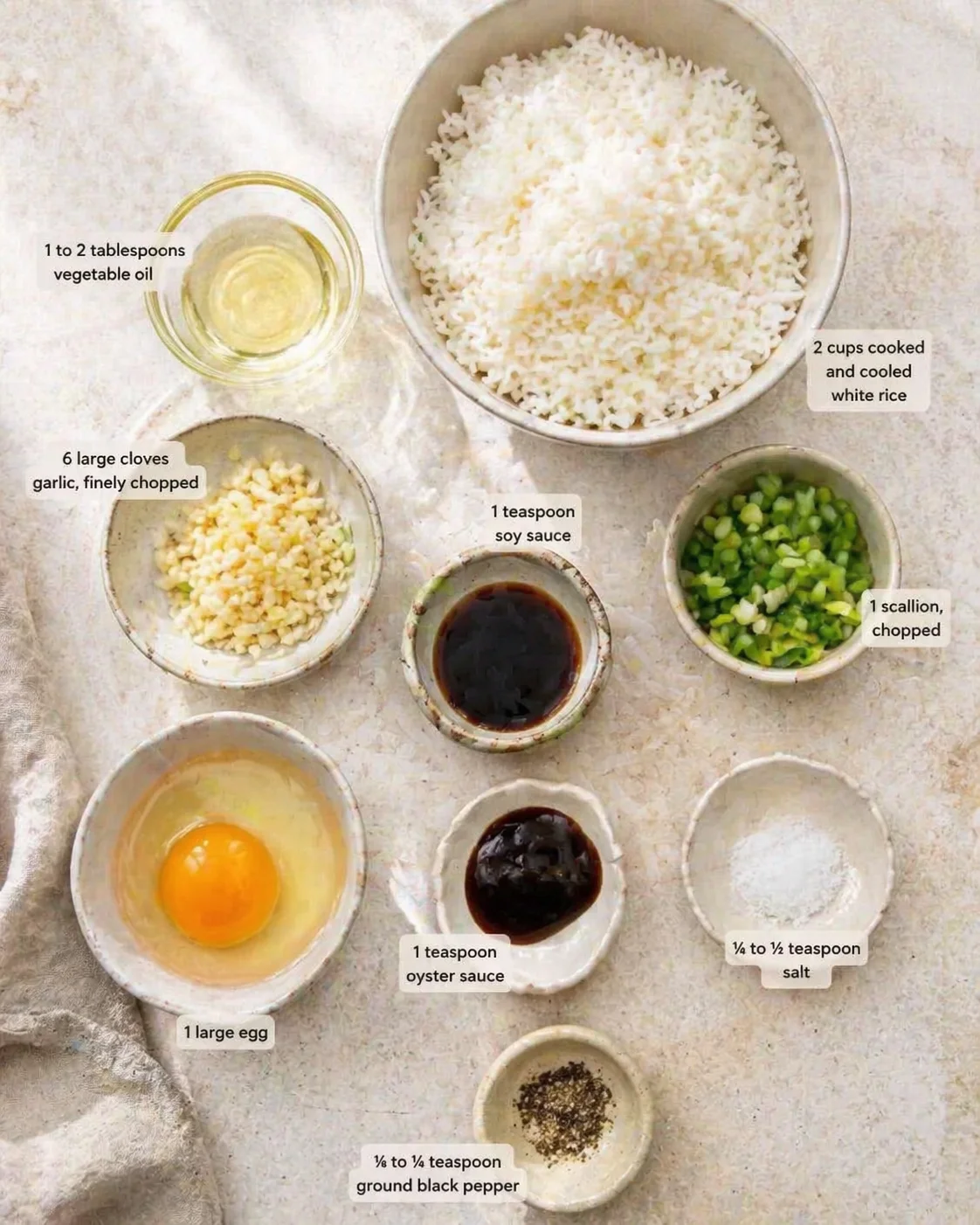 Overhead view of fried rice ingredients with bowls of rice, garlic, scallions, egg, sauces, and oil.