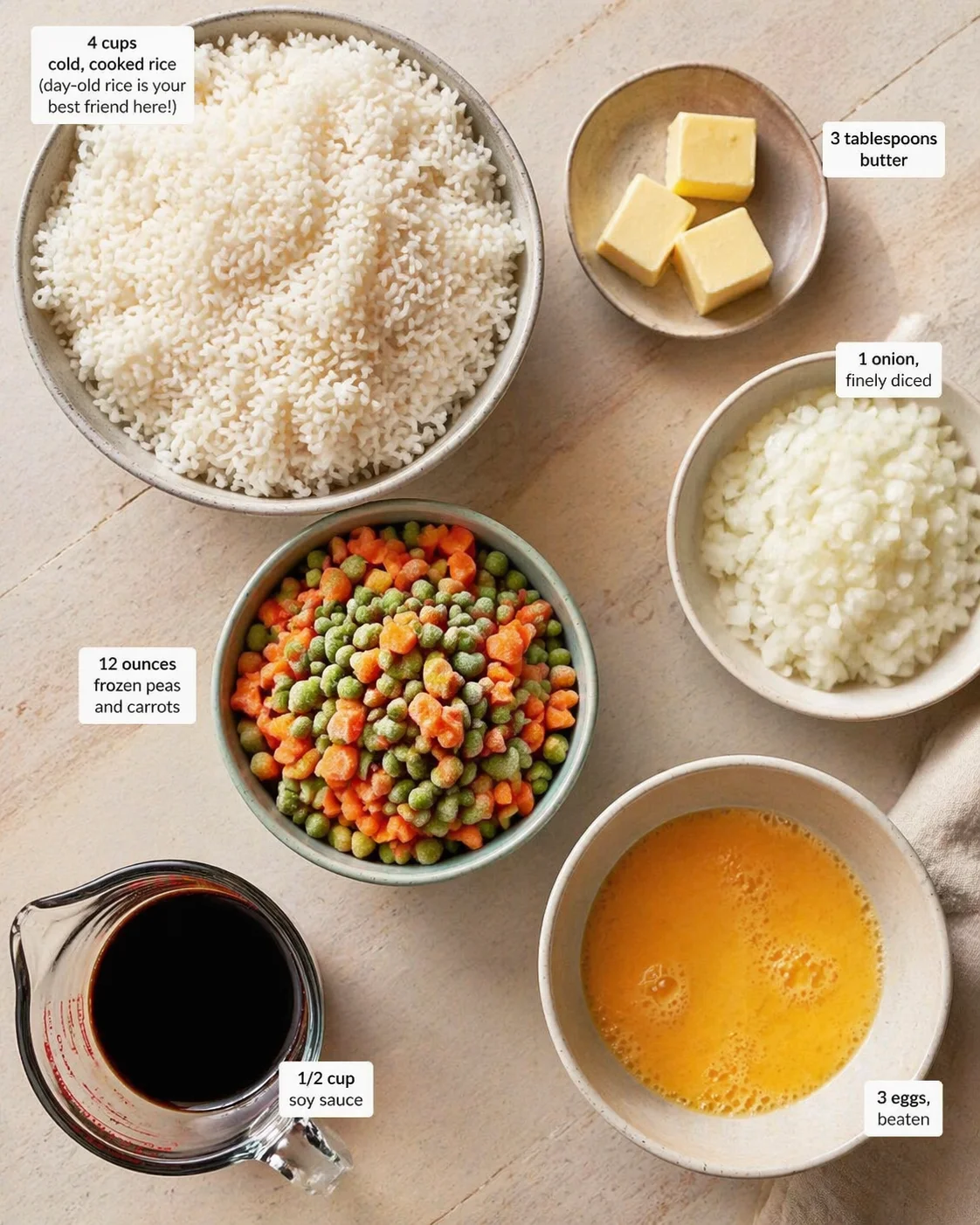 Overhead view of bowls with rice, onion, butter, peas and carrots, eggs, and soy sauce for fried rice.