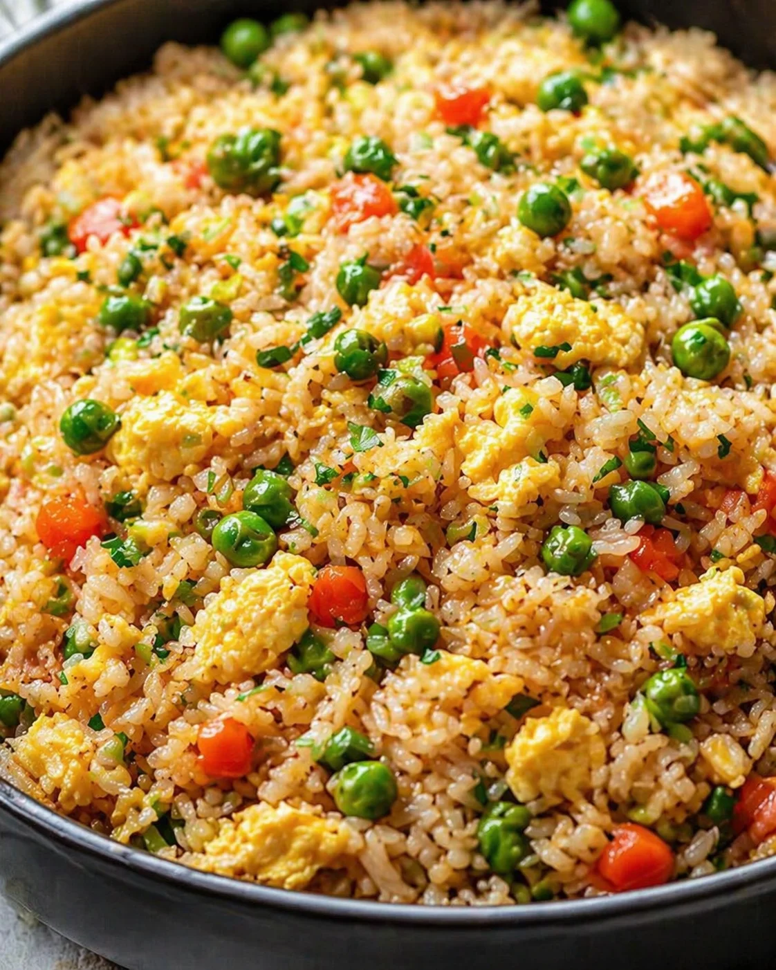 Close-up of fried rice with scrambled eggs, peas, and diced carrots in a skillet.