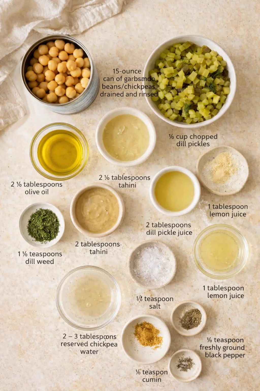 Overhead view of bowls containing chickpeas, diced pickles, chopped dill, tahini, olive oil, lemon juice, and spices.