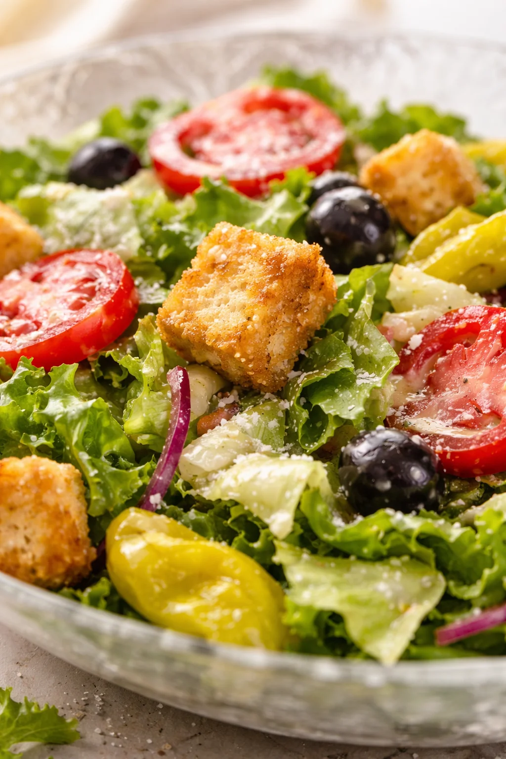bowl of mixed greens with tomato slices, olives, onions, yellow peppers, and crispy croutons
