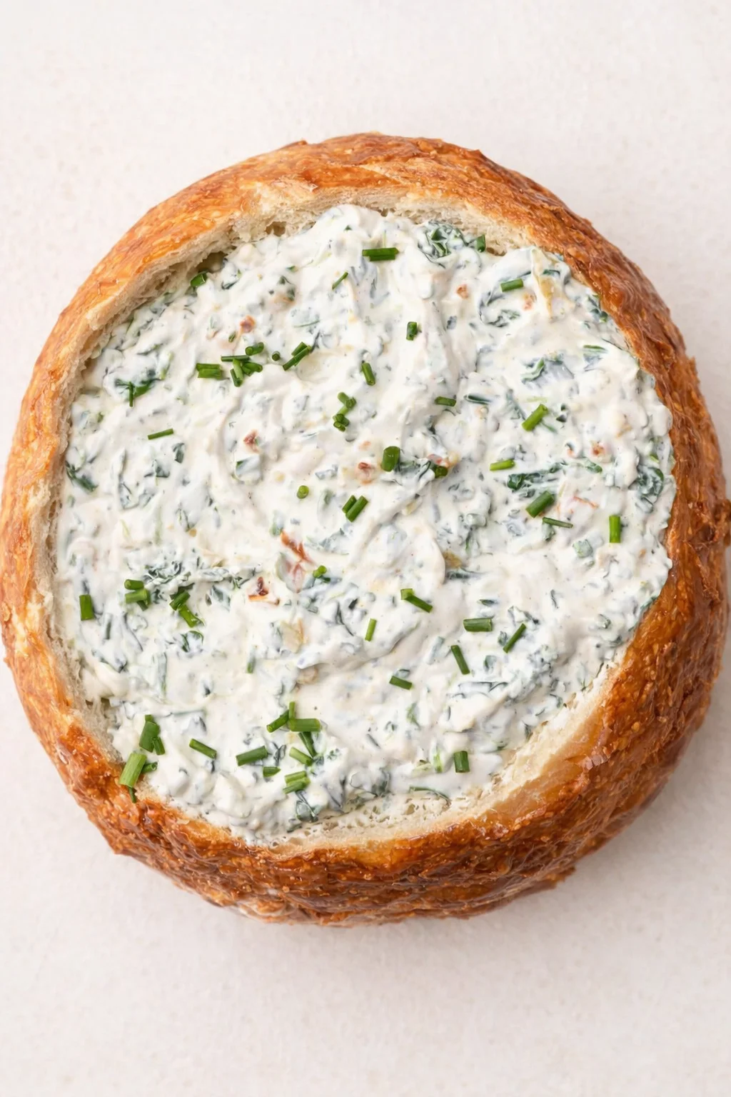 round crusty bread loaf hollowed and filled with creamy herb-cheese dip, sprinkled with chives.