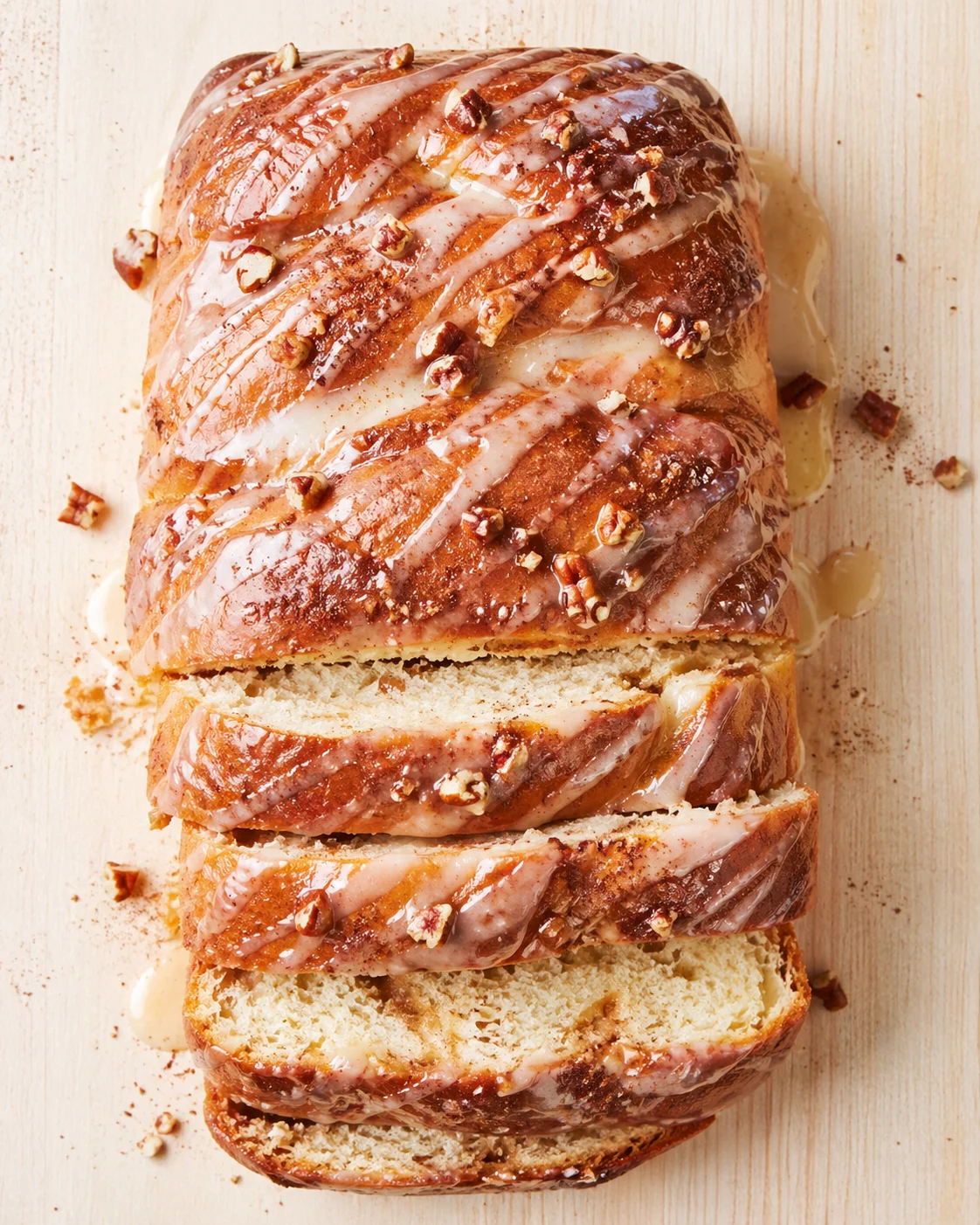 Glazed pecan-brioche loaf with drizzled icing and chopped pecans on a wooden board