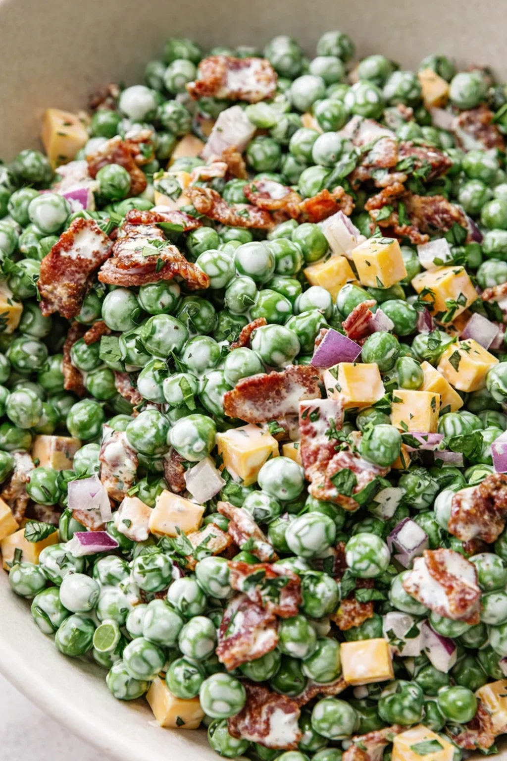 Close-up of green peas tossed with cheddar cheese cubes, bacon, red onion, and herbs in a creamy dressing