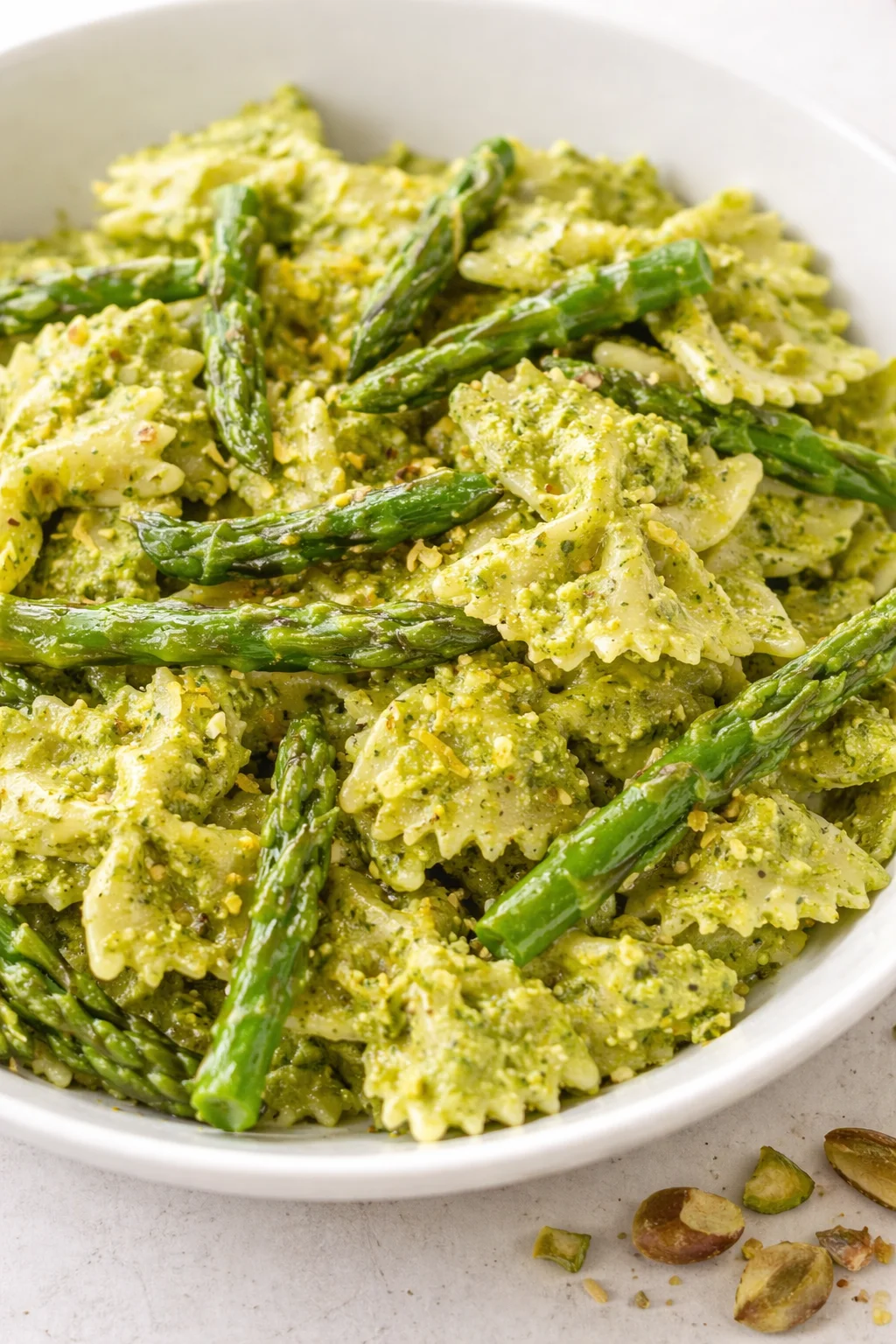 white bowl of bow-tie pasta with green pesto and asparagus spears