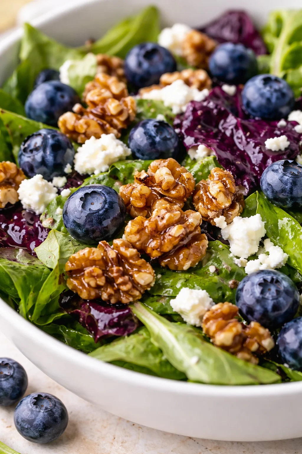 Vibrant mixed greens with blueberries, candied walnuts, and feta in a white bowl.