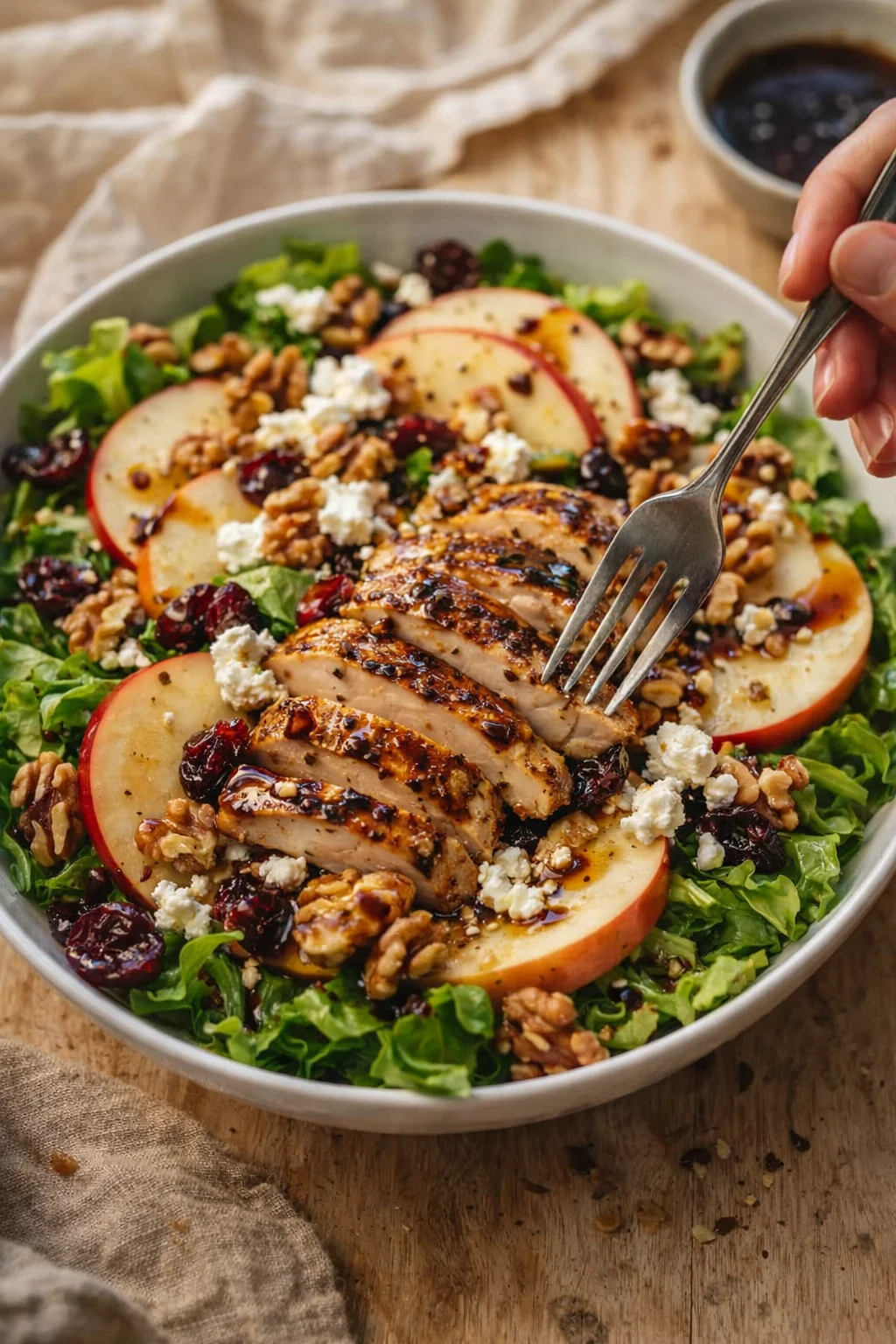 Sliced grilled chicken atop a mixed-greens salad with apple slices, walnuts, cranberries, and feta.