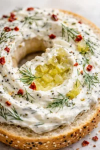 Seeded bagel ring topped with white herbed cream cheese, dill sprigs, red pepper flakes, and pineapple center.