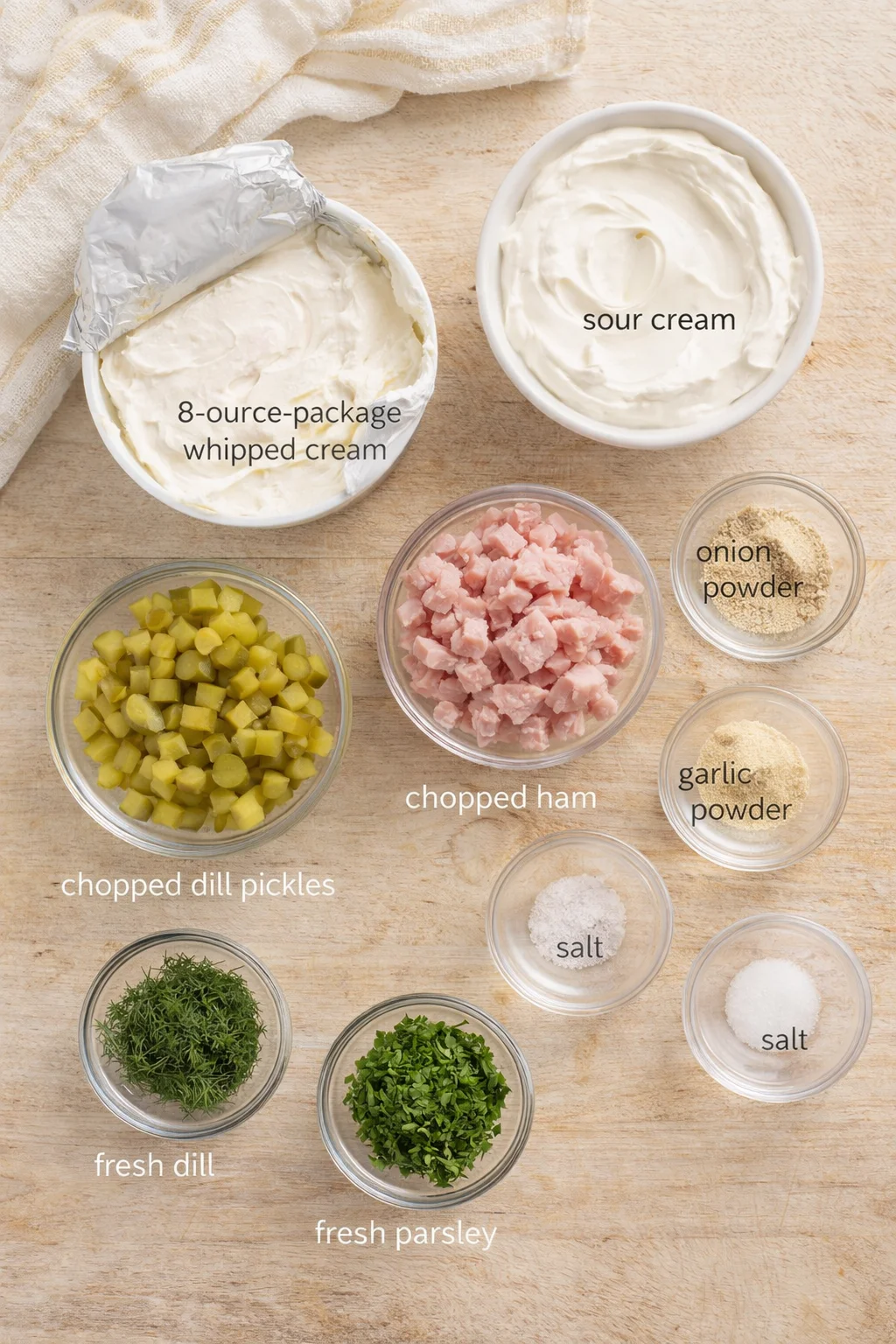 Top-down view of ingredient bowls with dairy, ham, pickles, herbs, and labeled powders.