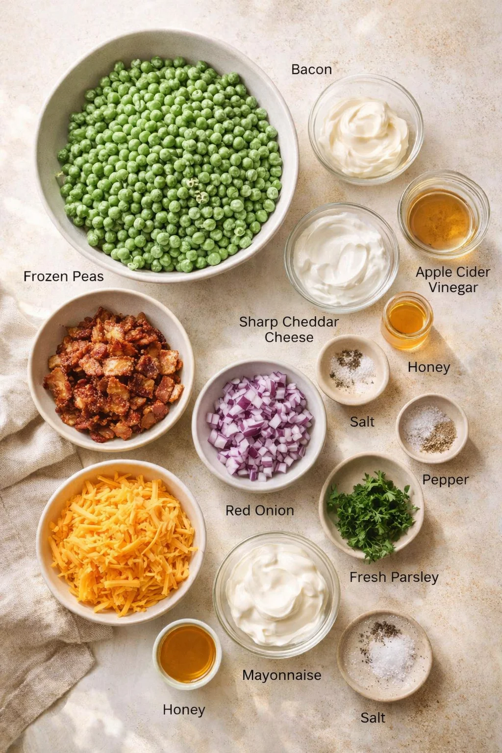 Overhead view of labeled ingredient bowls on a beige surface: peas, bacon, cheese, onion, mayo.