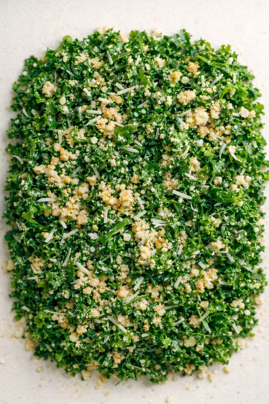 Close-up of finely chopped kale with crumbled breadcrumbs and shredded Parmesan on a light background