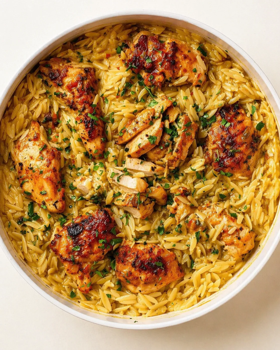 Top-down view of orzo pasta with grilled chicken pieces, garnished with parsley.