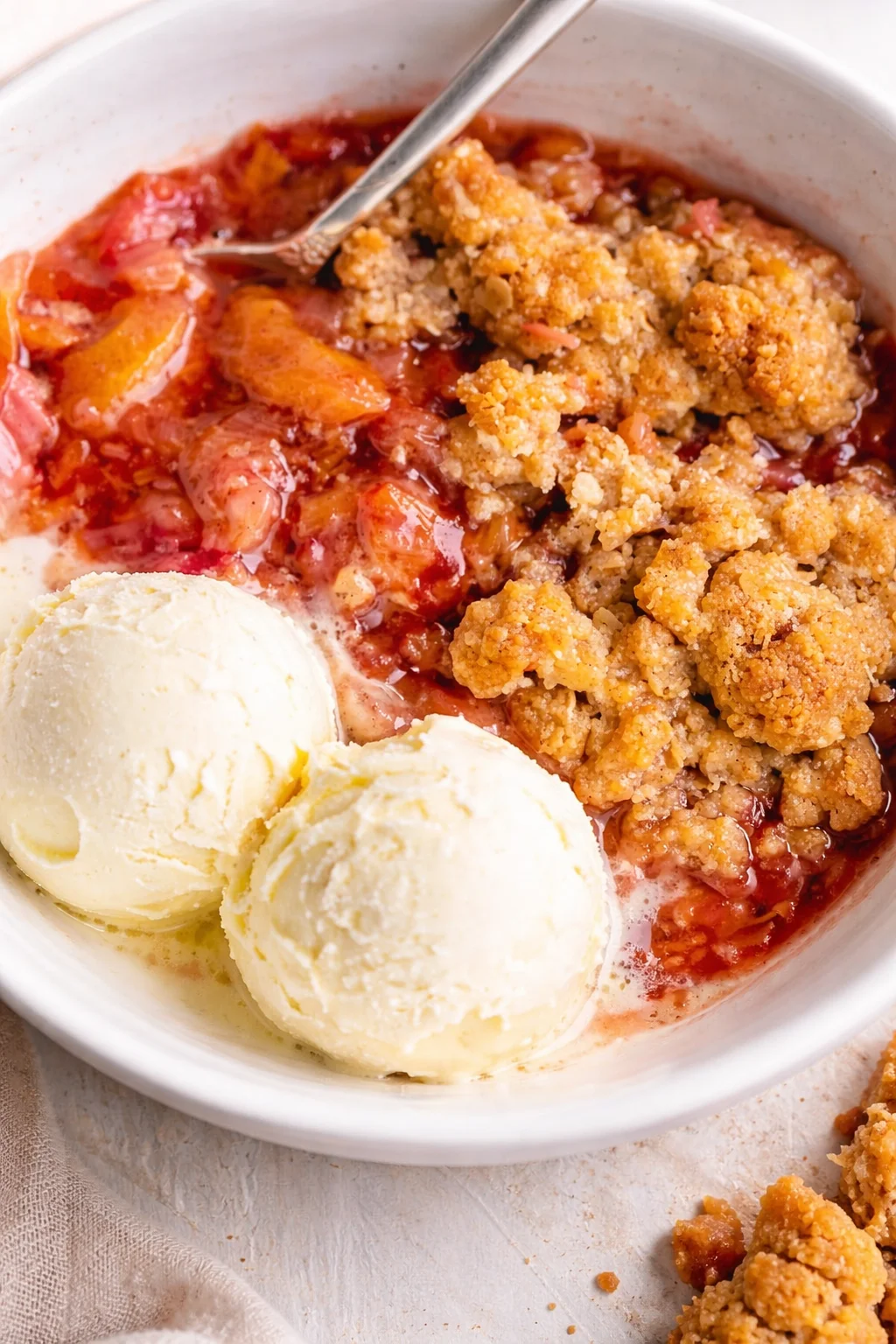 bowl of warm peach-berry crumble with two scoops vanilla ice cream