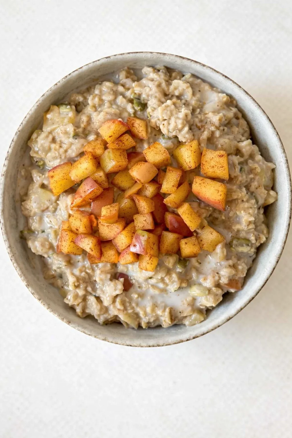 Top-down view of creamy oatmeal topped with diced peaches in a rustic ceramic bowl