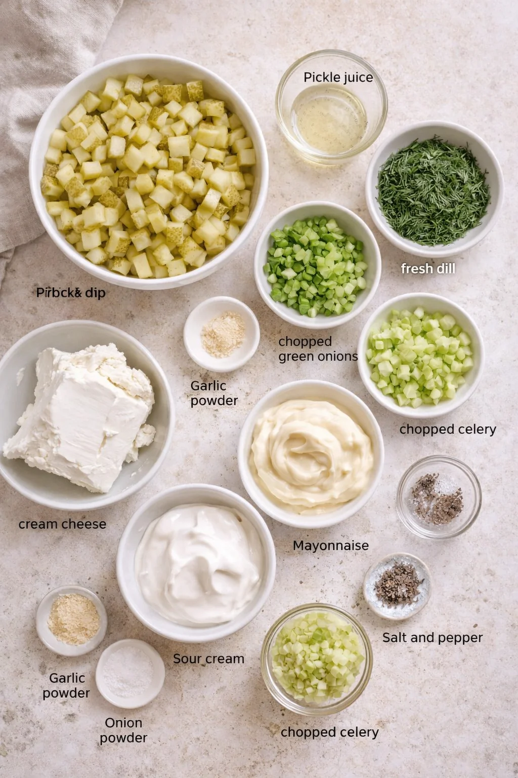 overhead view of ingredients for pickle dip arranged in bowls on a beige countertop