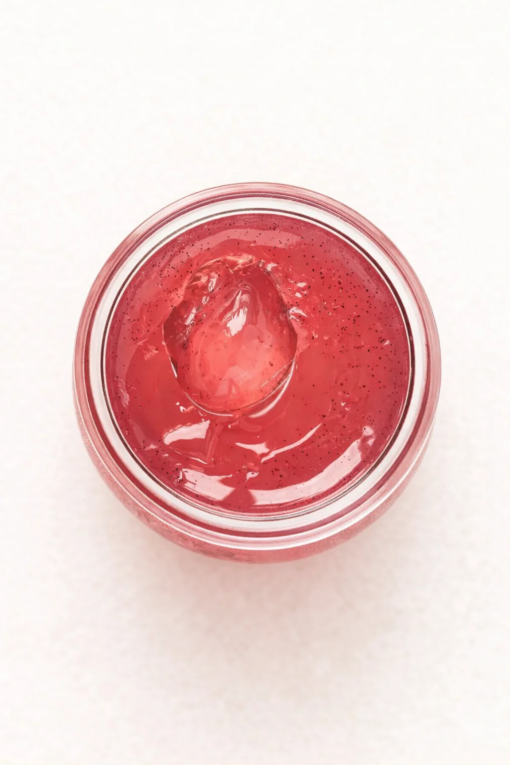 Top-down view of a pink smoothie with an ice cube in a mason jar on a pale background.